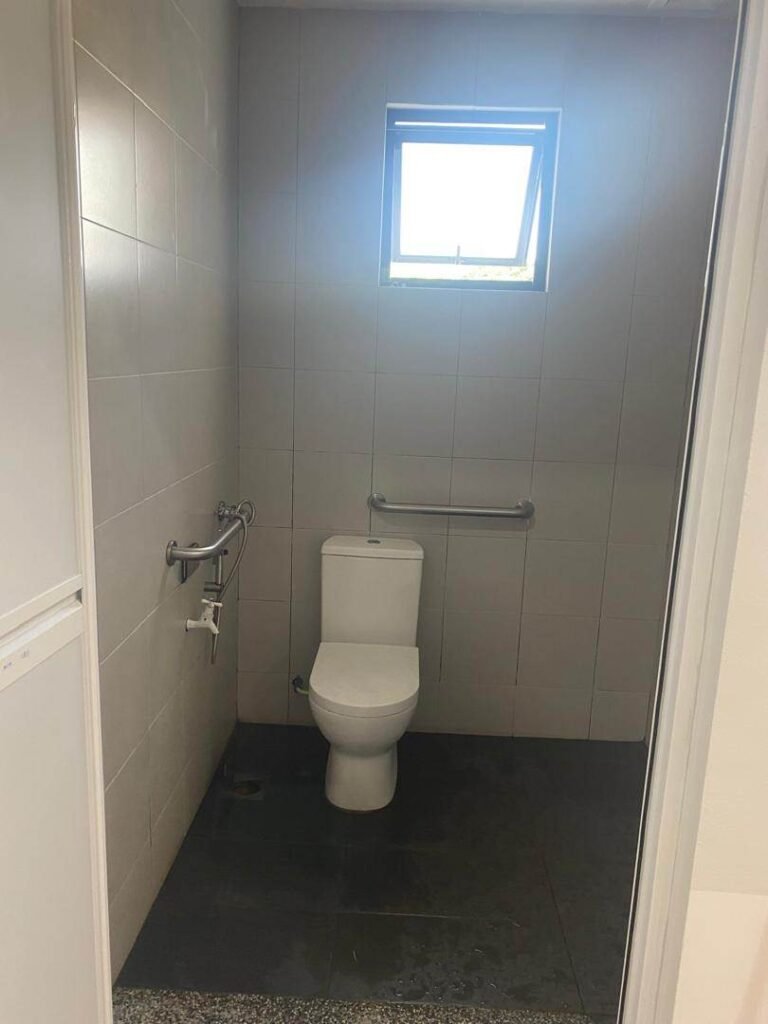 Accessible bathroom renovation with grab bars, tiled walls, and natural lighting in Malaysia.