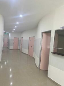 Clinic hallway renovation with dispensary sign, tiled flooring, and emergency exit in Malaysia.