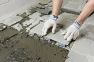 Worker installing ceramic bathroom floor tiles with mortar and spacers.